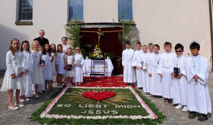 Die Kommunionkinder und Pfarrer Schemmerer bewundern  den Blumenteppich